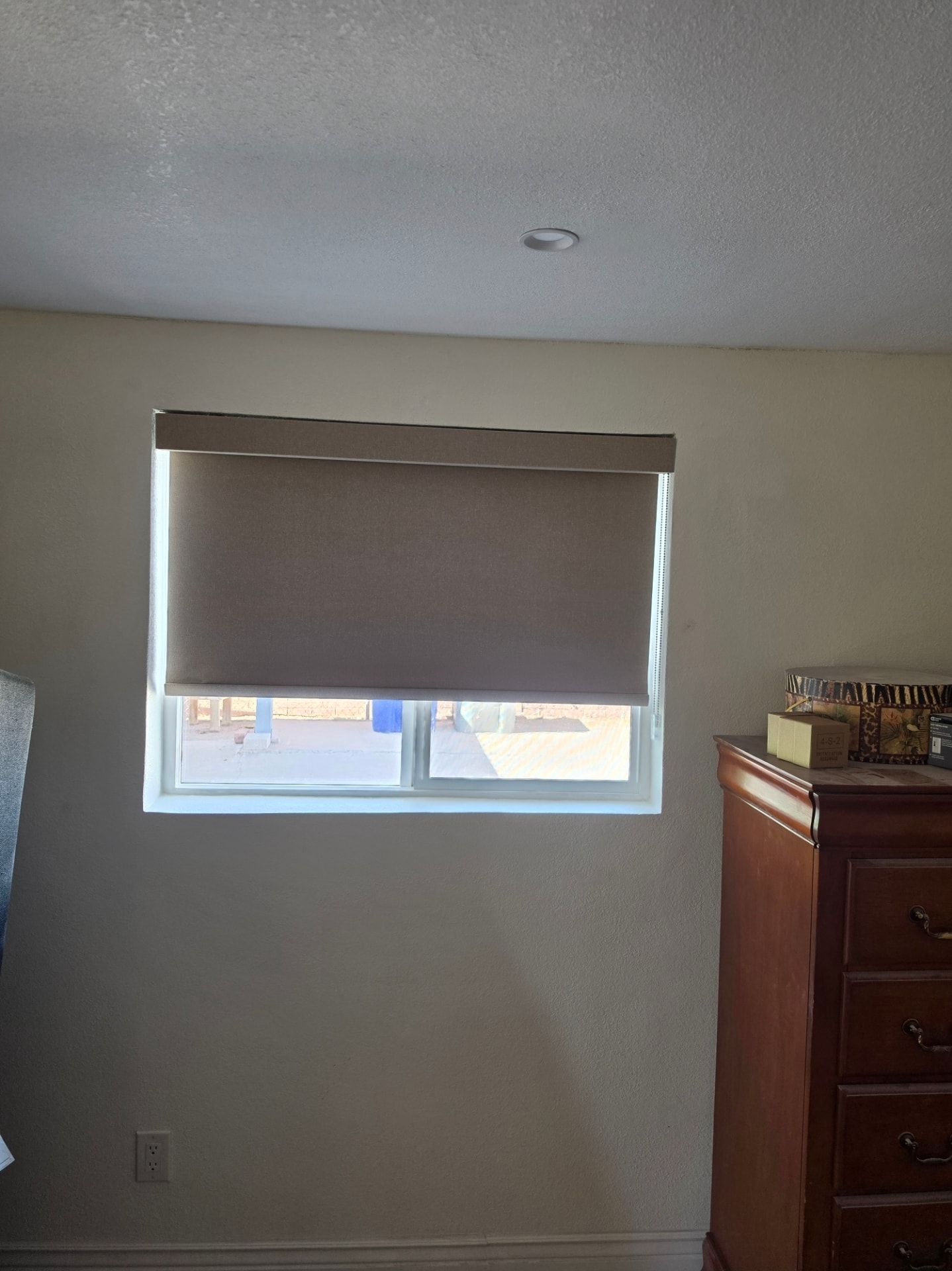 Taupe roller shade on a bedroom window next to a dresser